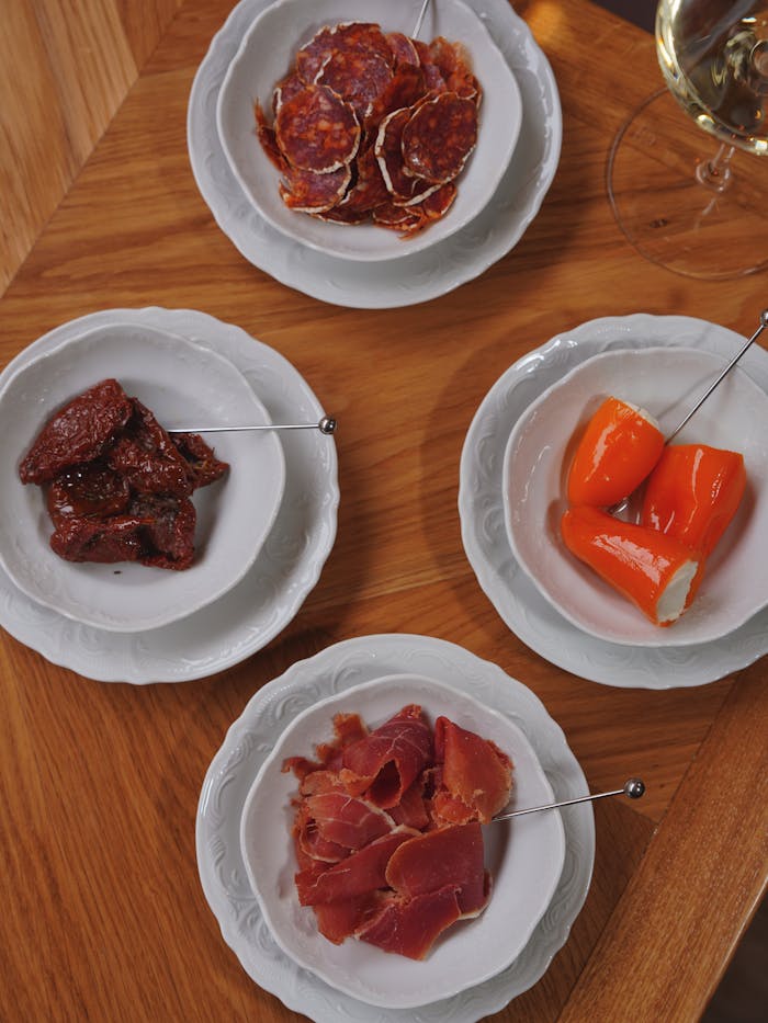 A top view of a gourmet tapas platter featuring cured meats and stuffed peppers on a wooden table.