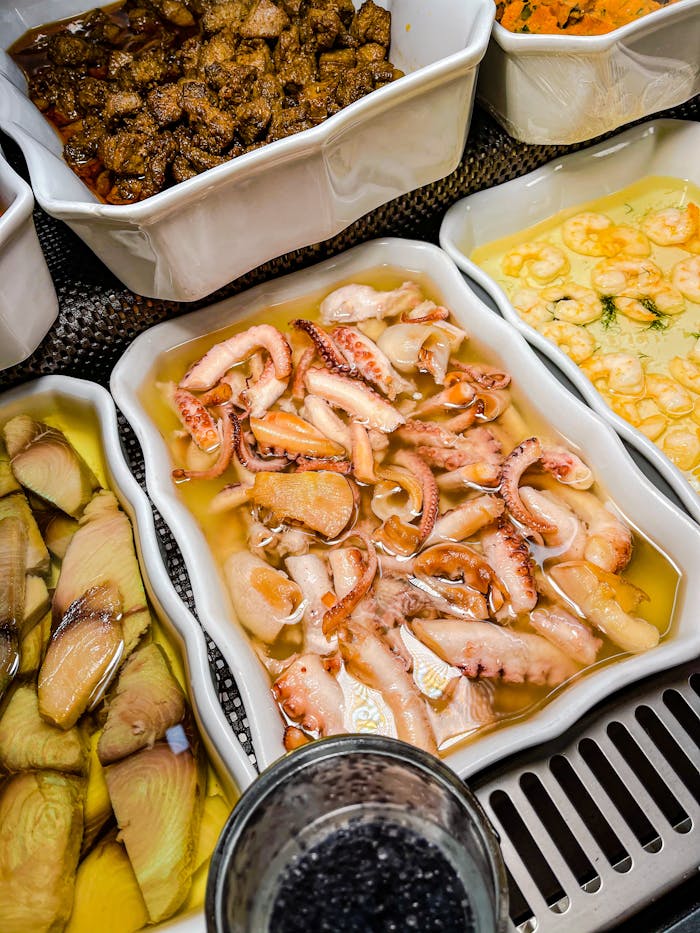 Variety of fresh seafood appetizers including calamari and shrimp served in white trays.